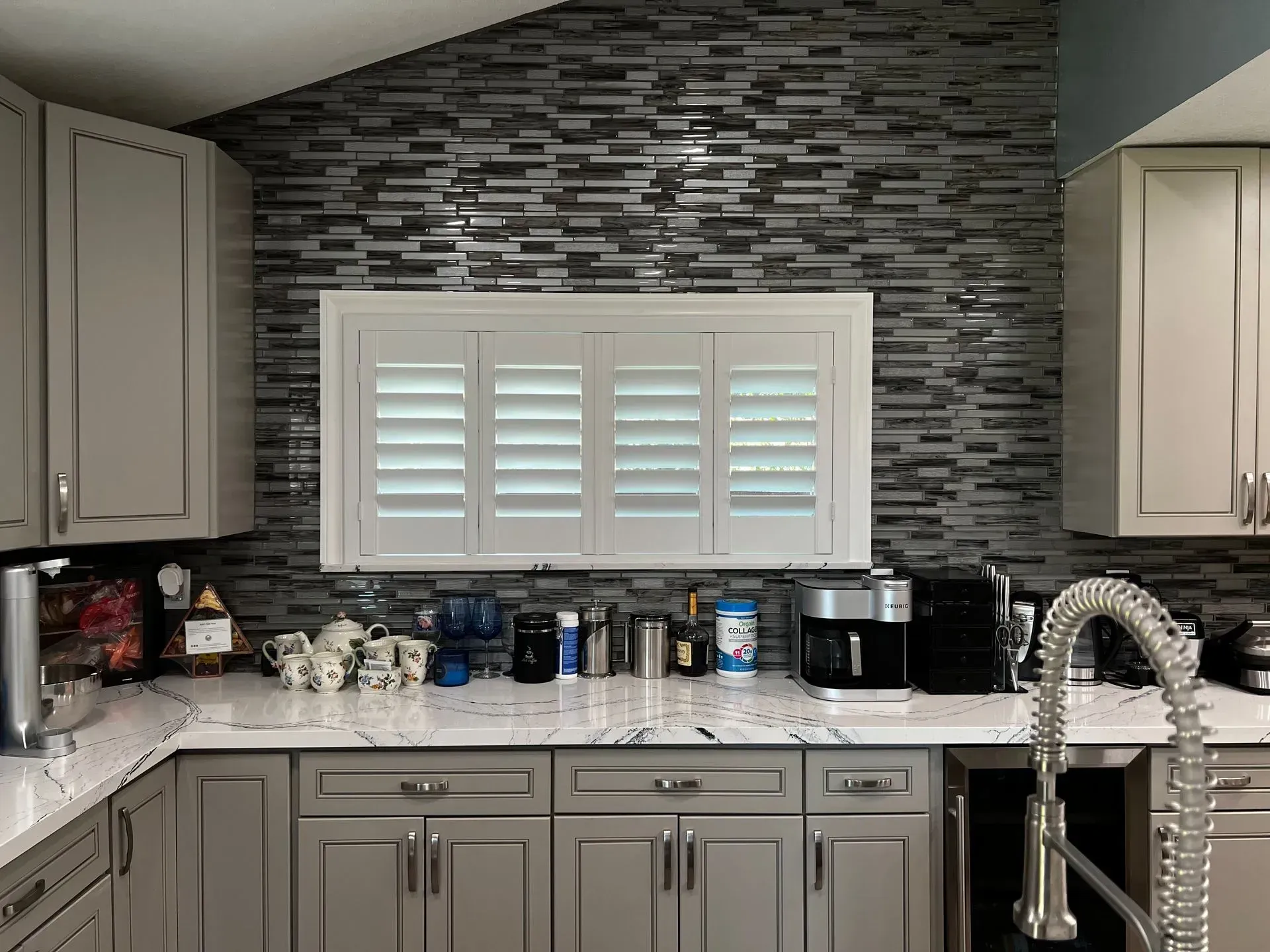 A kitchen with gray cabinets , white counter tops , a sink and a window.