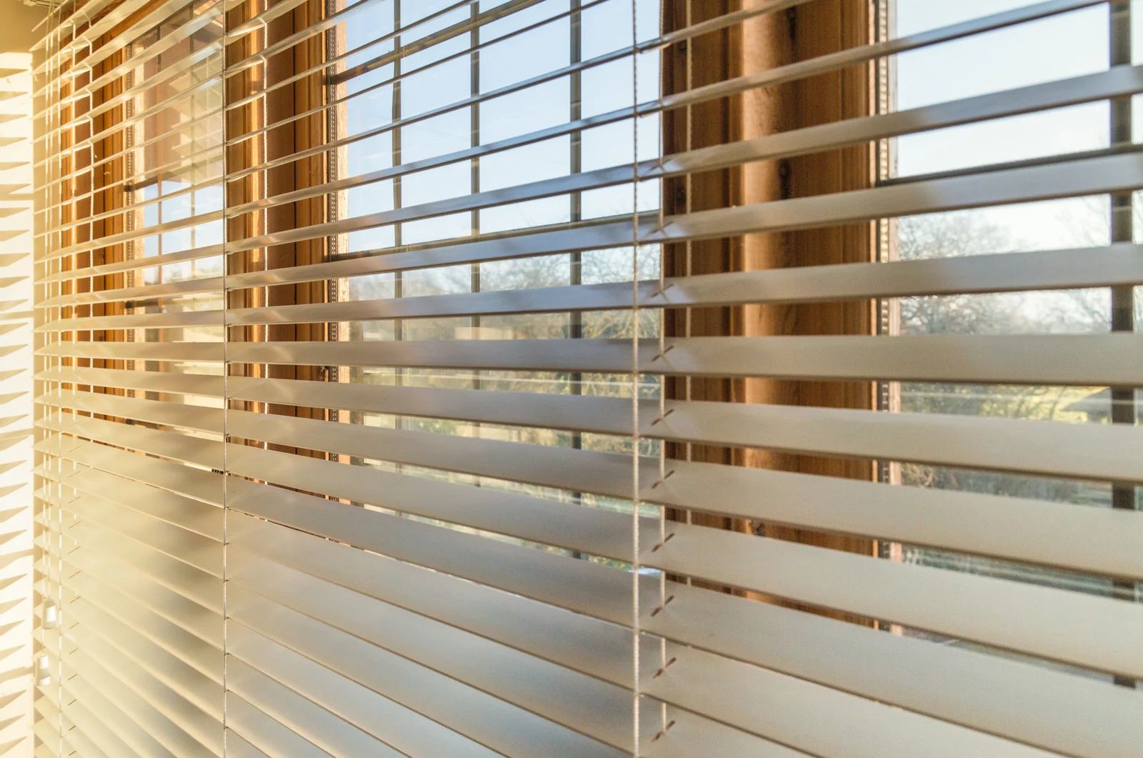 Closed, light-colored blinds on a window, letting in sunlight.