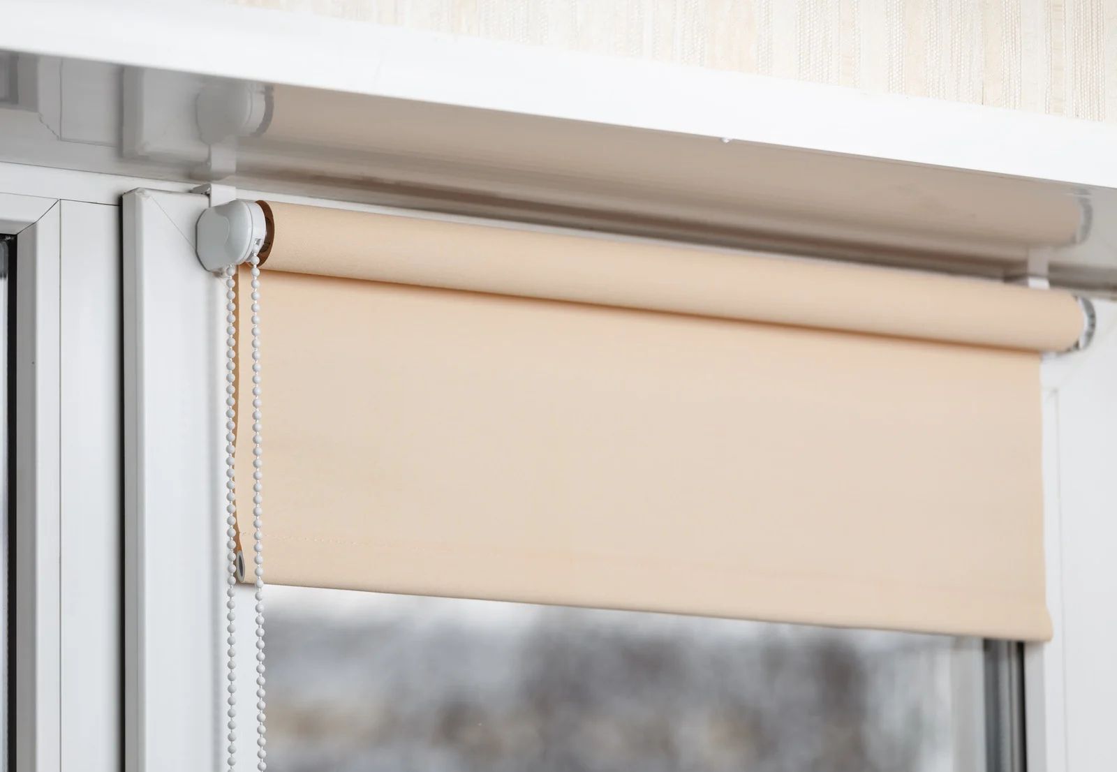 Tan roller blind partially covering a window, inside a white frame.