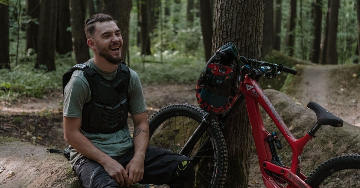 A man is sitting next to a bicycle in the woods.