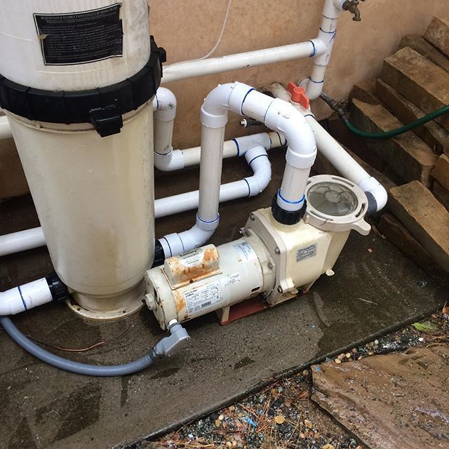 A swimming pool pump is attached to a white pipe