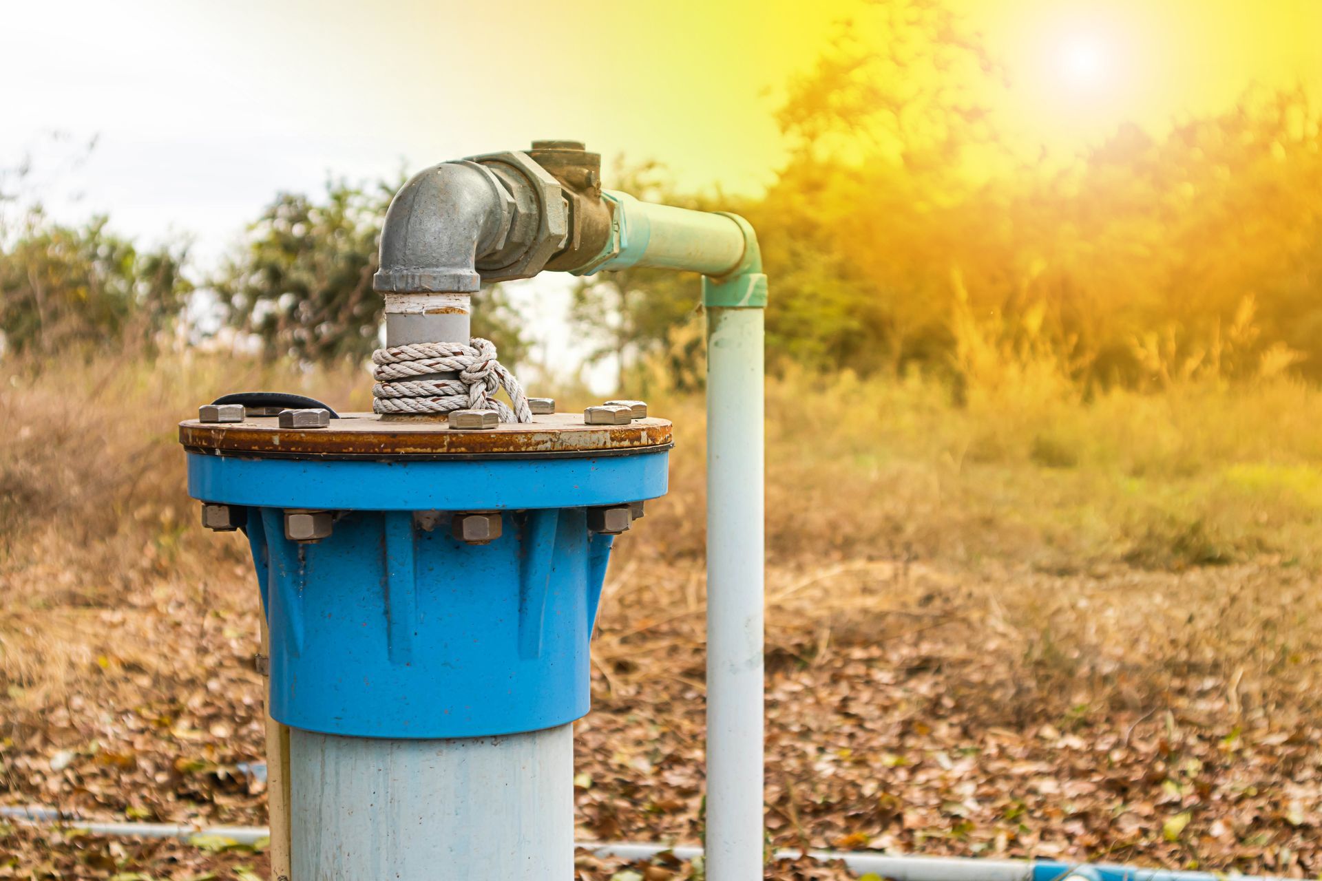 A blue metal wellhead pump connection stands in a dry field at sunset. A blue metal wellhead pump connection stands in a dry field at sunset.