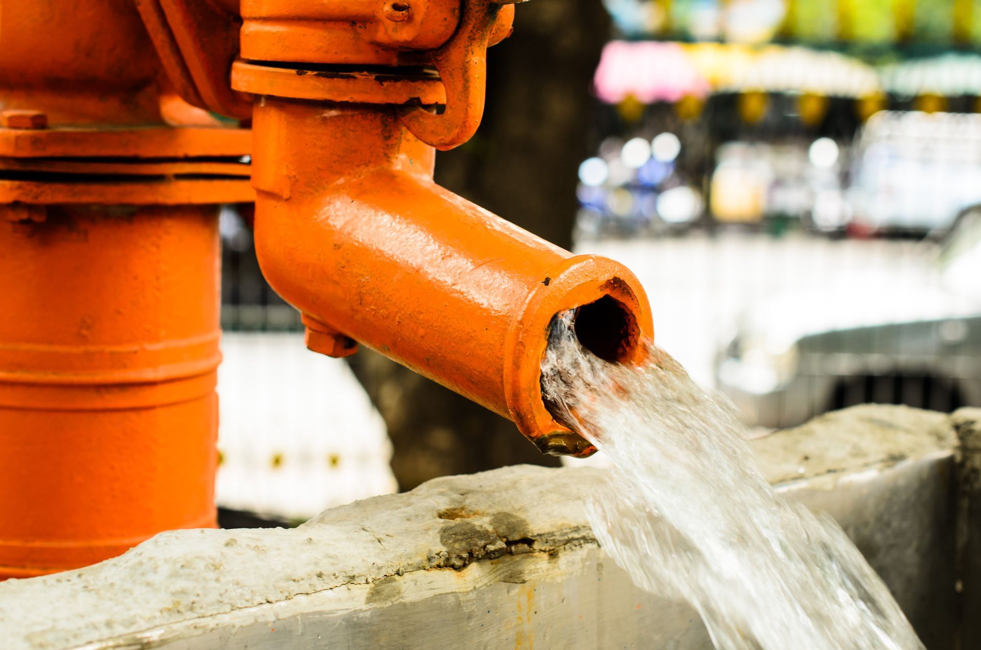 Water flows steadily from an orange metal pump into a concrete basin.