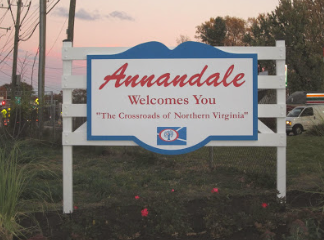 A white welcome sign for Annandale, Virginia, featuring red text and a small emblem, set outdoors at dusk.