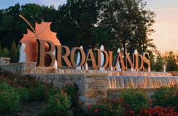Broadlands entrance sign with stone wall, flowers, and trees at sunset