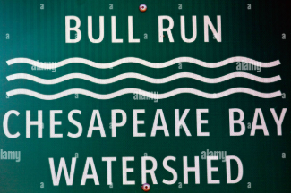A metal agricultural irrigation valve with a red handle, situated in a field next to a patch of green crops. A metal agricultural irrigation valve with a red handle, situated in a field next to a patch of green crops.
