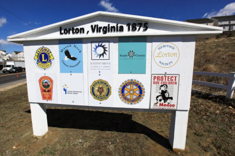A white, gabled sign in Lorton, Virginia, displays ten various community organization logos on a sunny, outdoor grassy hill. A white, gabled sign in Lorton, Virginia, displays ten various community organization logos on a sunny, outdoor grassy hill.