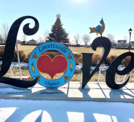 Aerial view of a white house with a green lawn, circular driveway, and surrounding trees