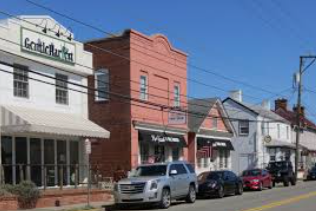Small-town street with colorful storefronts, parked cars, and a clear blue sky