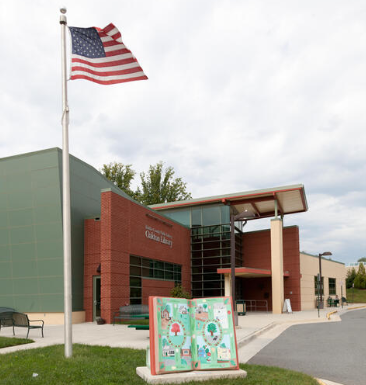 A brick library building with a flagpole, American flag, and an open book sculpture on the front lawn. A brick library building with a flagpole, American flag, and an open book sculpture on the front lawn.
