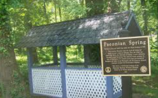 Wooden spring shelter in a wooded area with a sign reading “Paconian Spring”