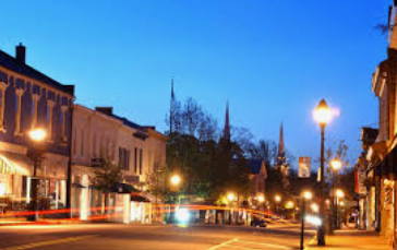 Aerial view of a white house with a green lawn, circular driveway, and surrounding trees