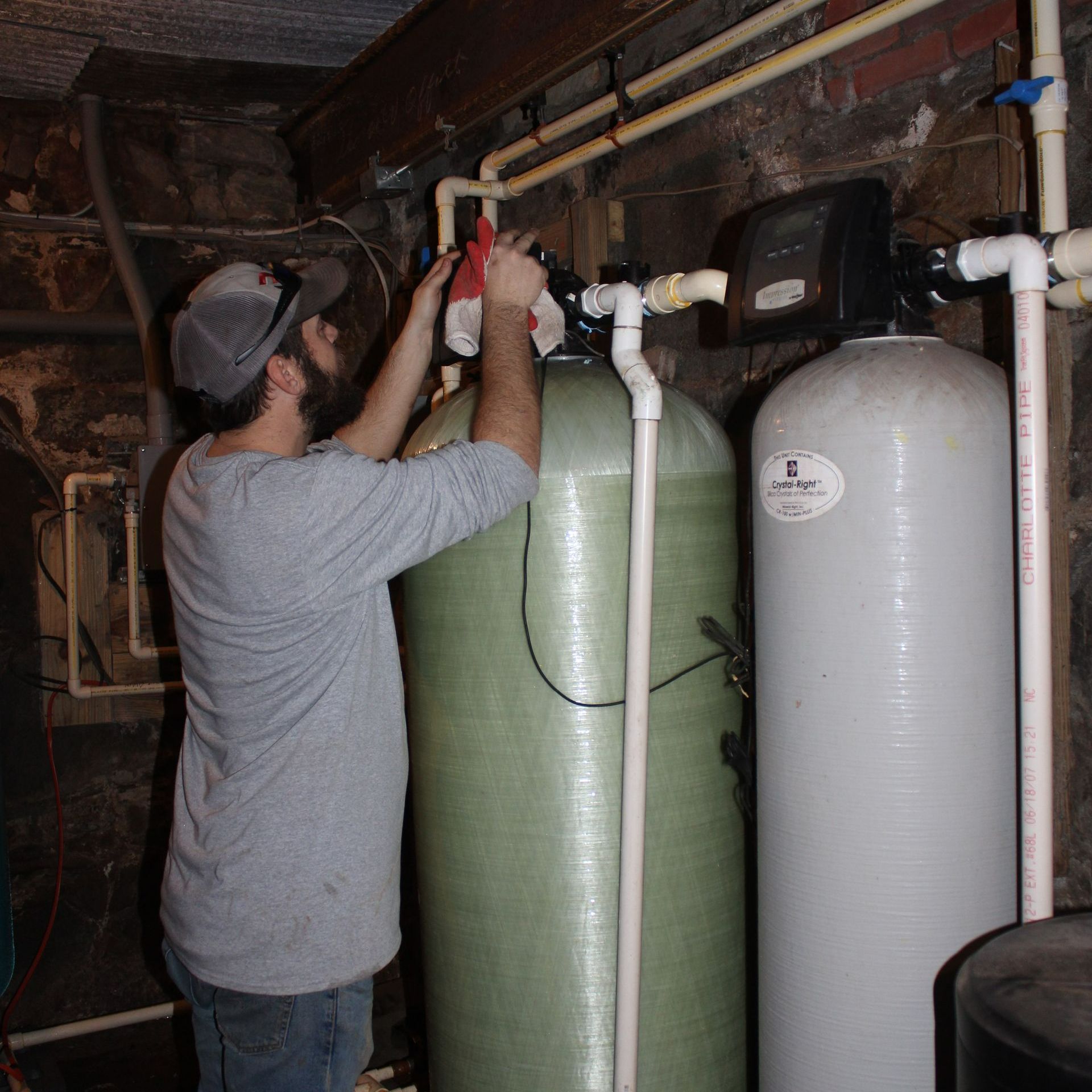 Man in a gray shirt working on water filtration system in a basement.