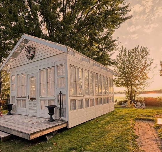 Véranda blanche donnant sur un lac au coucher du soleil, avec un petit porche et un chemin menant aux chaises.