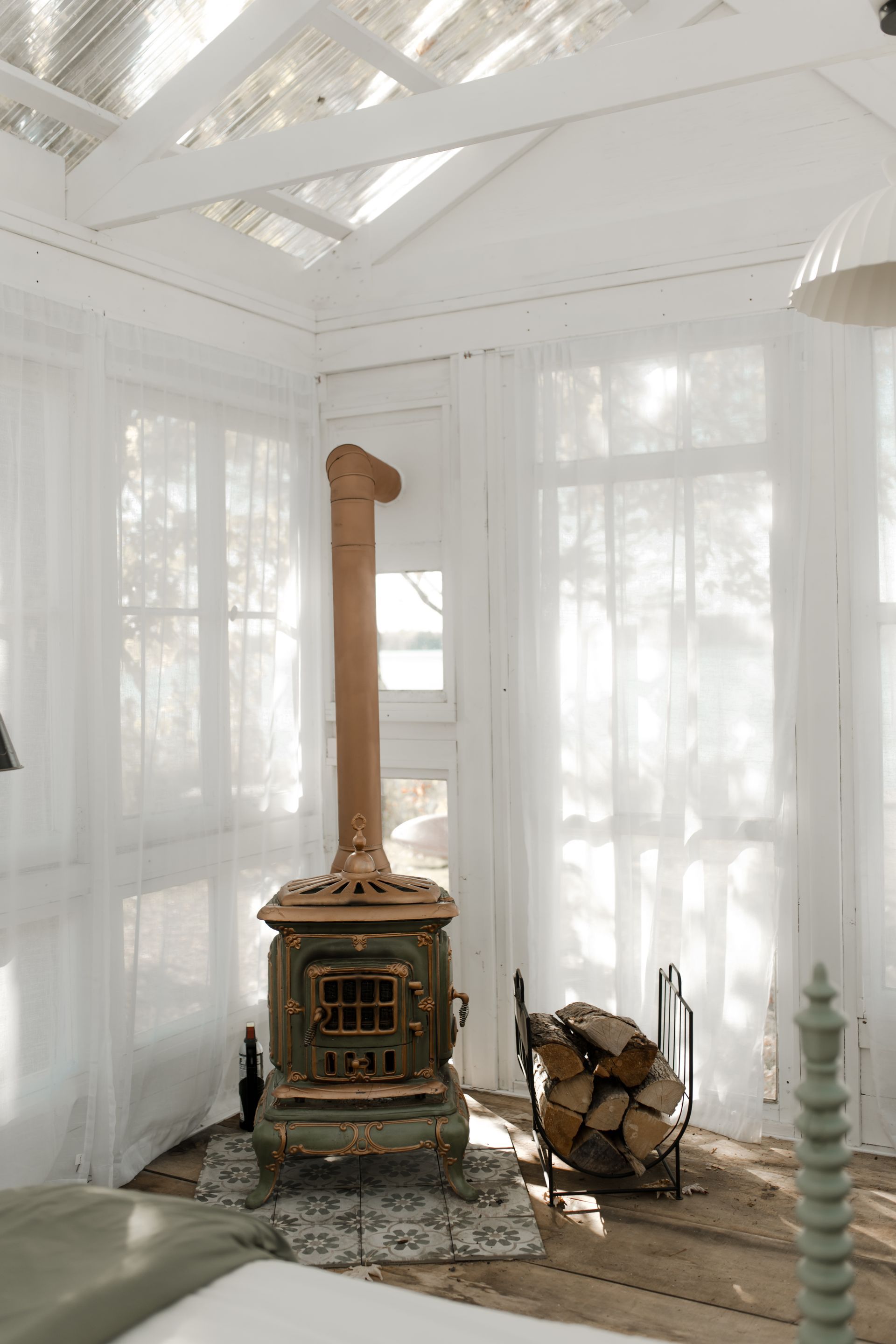 Un poêle vert vintage aux accents cuivrés se dresse dans une pièce lumineuse aux rideaux transparents, deux décorations en forme de flamants roses se trouvent à proximité.