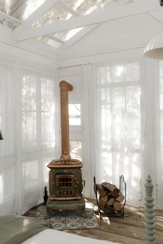 Un poêle vert vintage aux accents cuivrés se dresse dans une pièce lumineuse aux rideaux transparents, deux décorations en forme de flamants roses se trouvent à proximité.