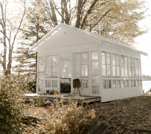 Véranda blanche avec fenêtres et porche, sur une pelouse herbeuse près de l'eau.