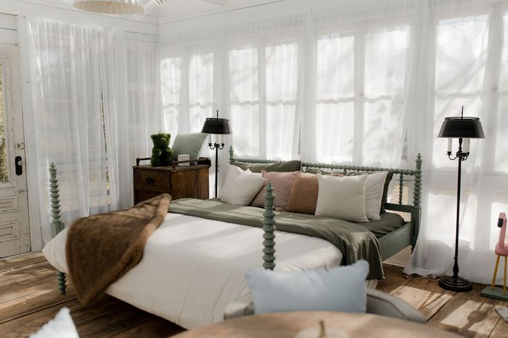 Chambre douillette avec lit, voilages et verrière. Parure de lit verte, couverture en fourrure marron et coussins cœurs.