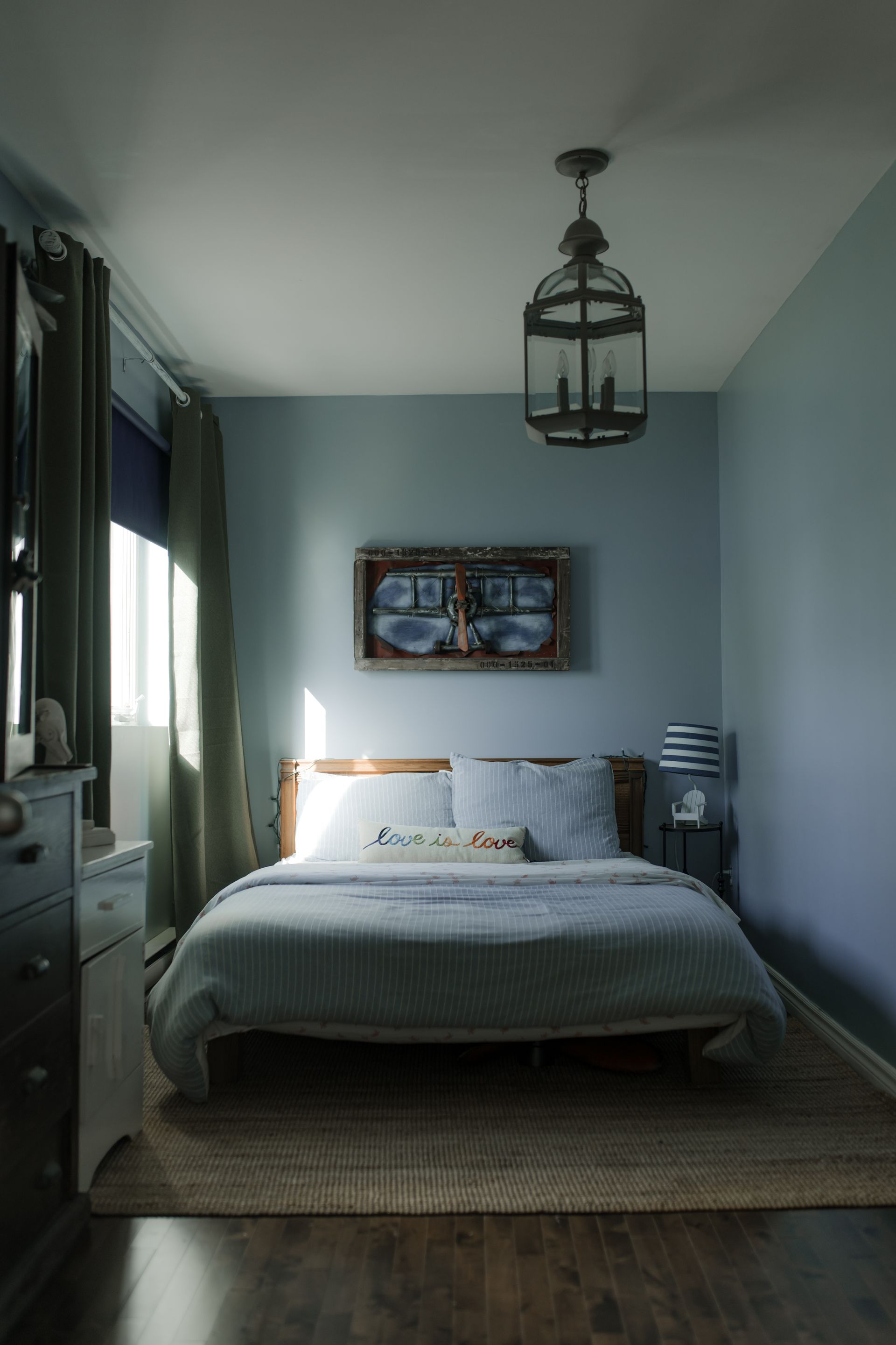 Chambre cosy avec lit, œuvres d'art, fenêtre et suspension. Éclairage tamisé et tons terre.