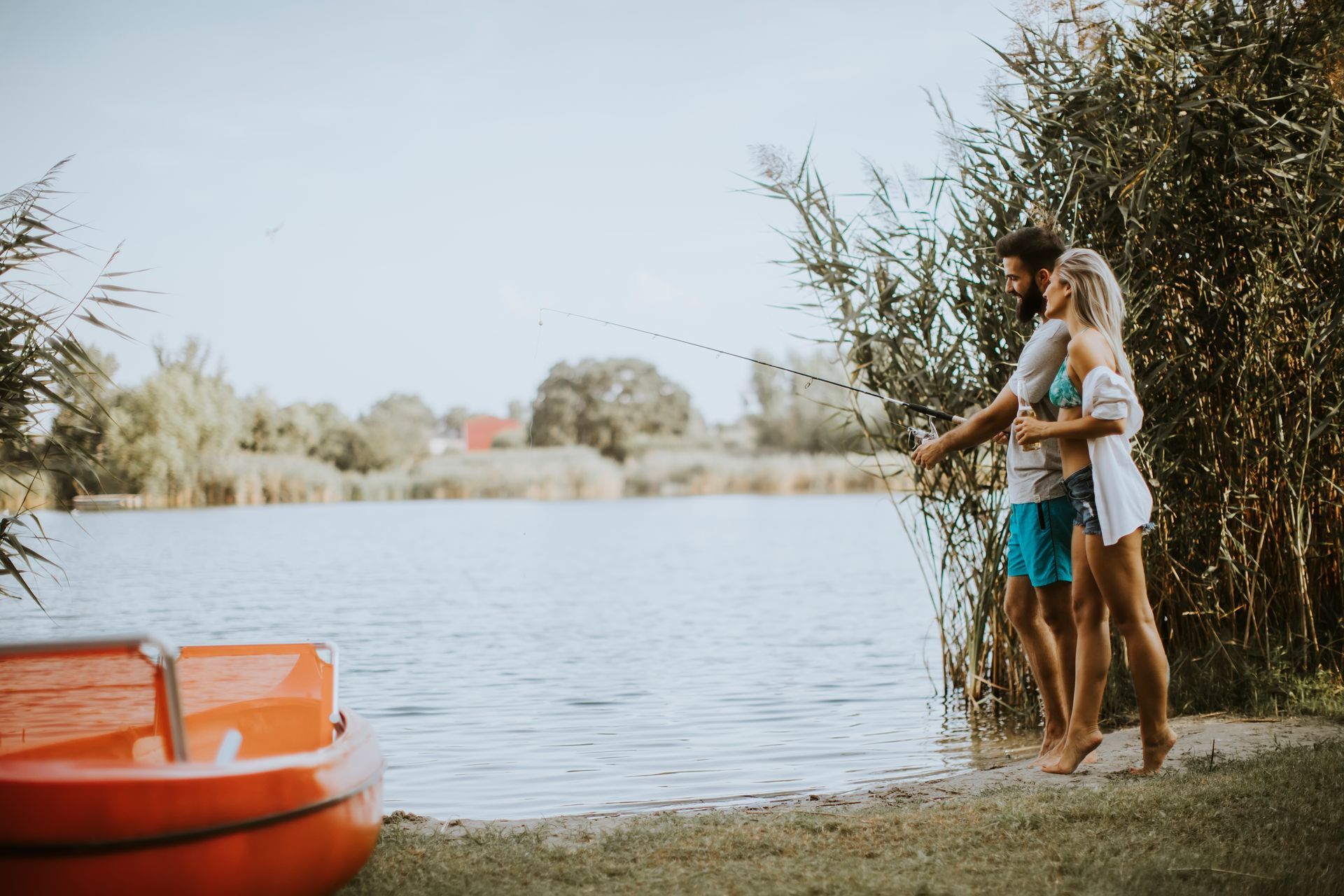 Couple pêchant au bord d'un lac, avec un bateau orange au premier plan.