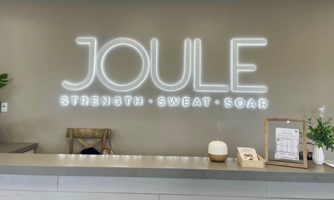The front desk of a gym with a neon sign that says `` joule ''.