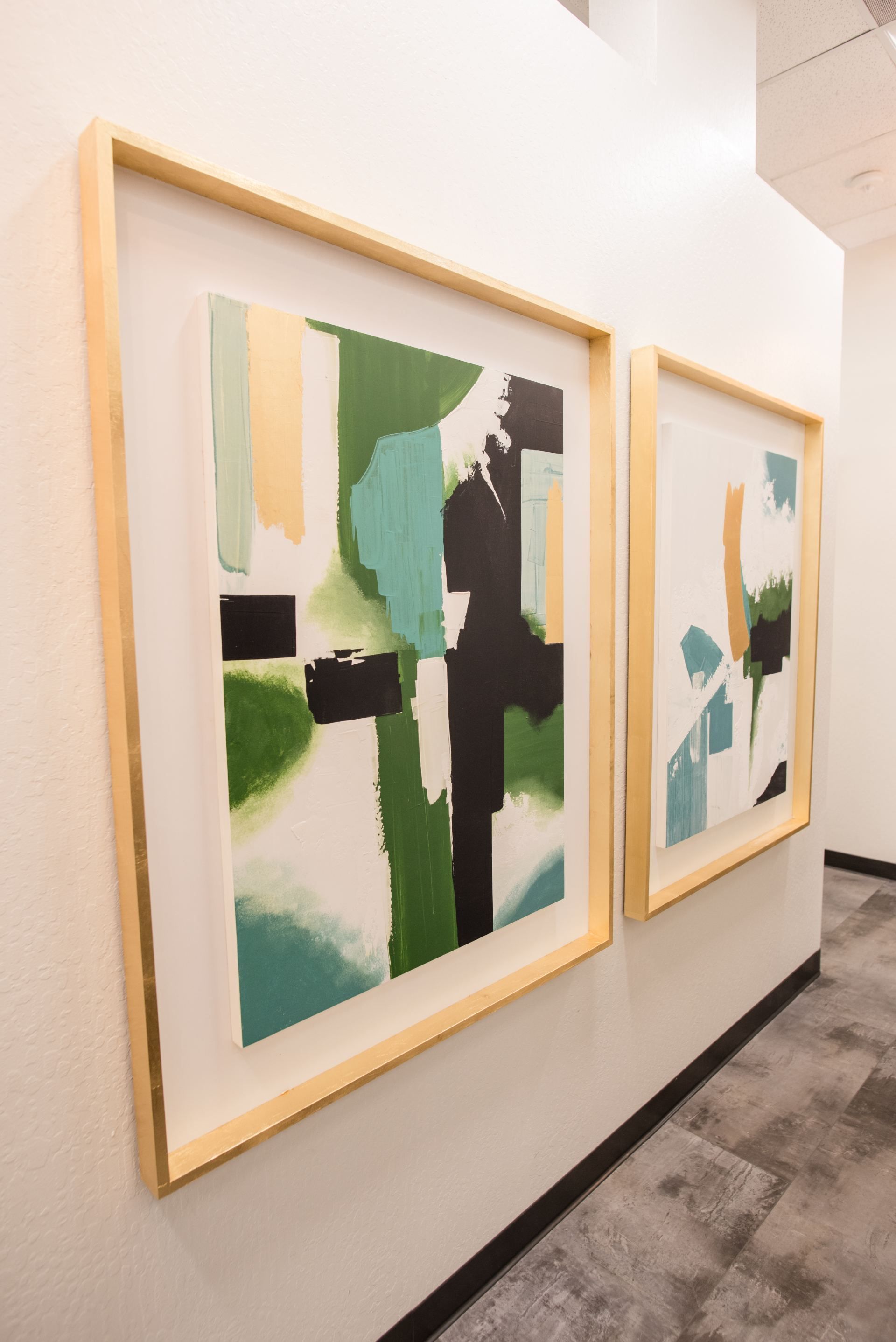 Two paintings are hanging on a wall in a hallway.