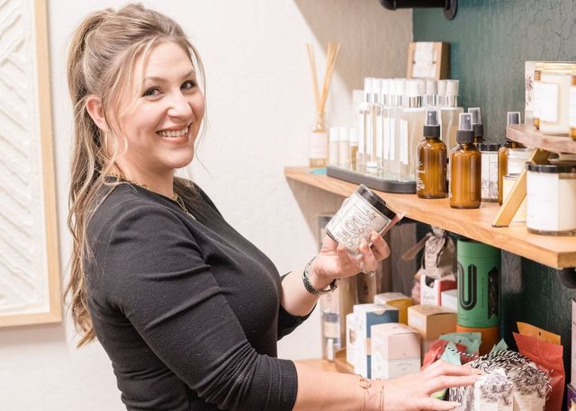 A woman is standing in front of a shelf holding a jar of candles.