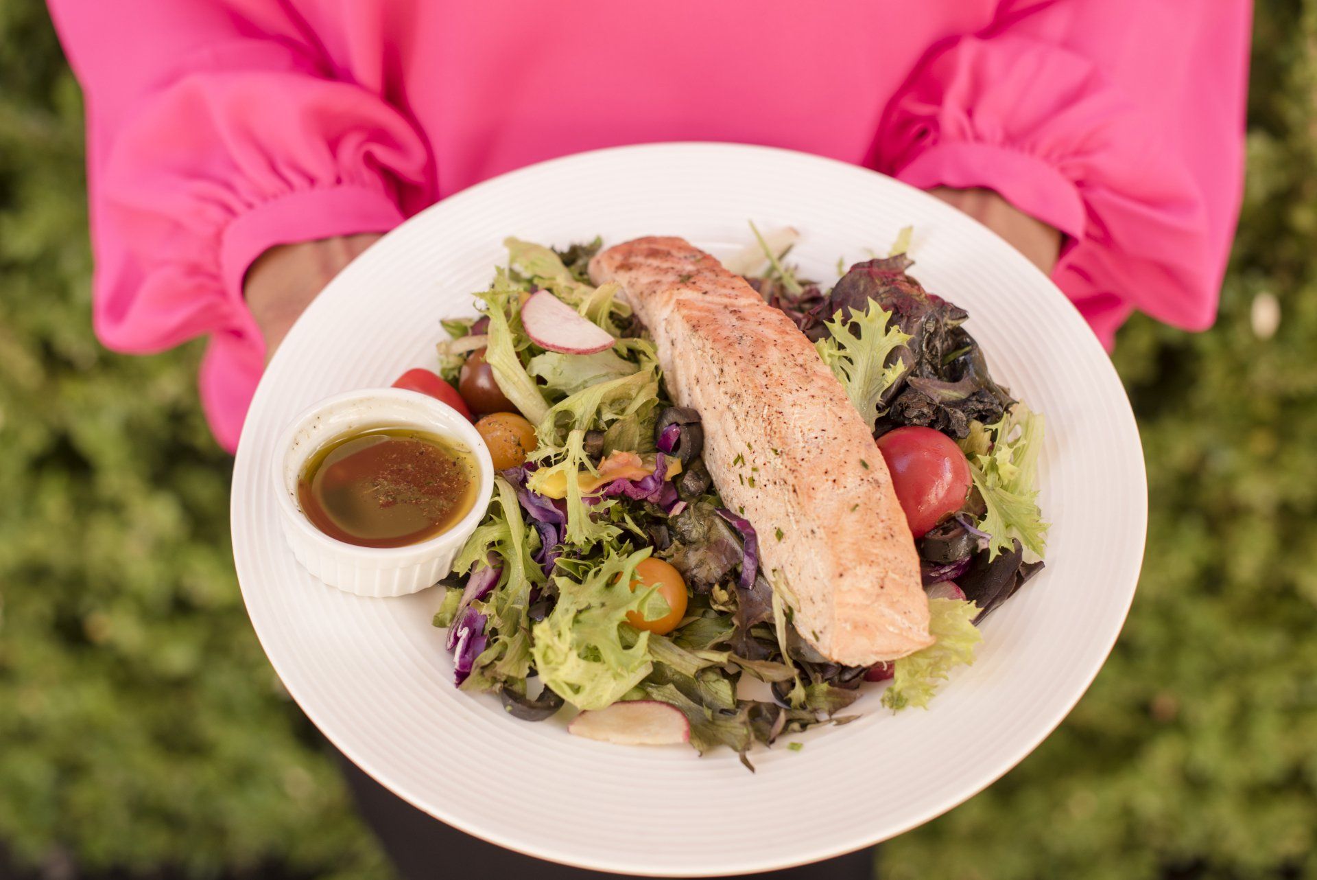 A woman is holding a plate of food with salmon and vegetables.