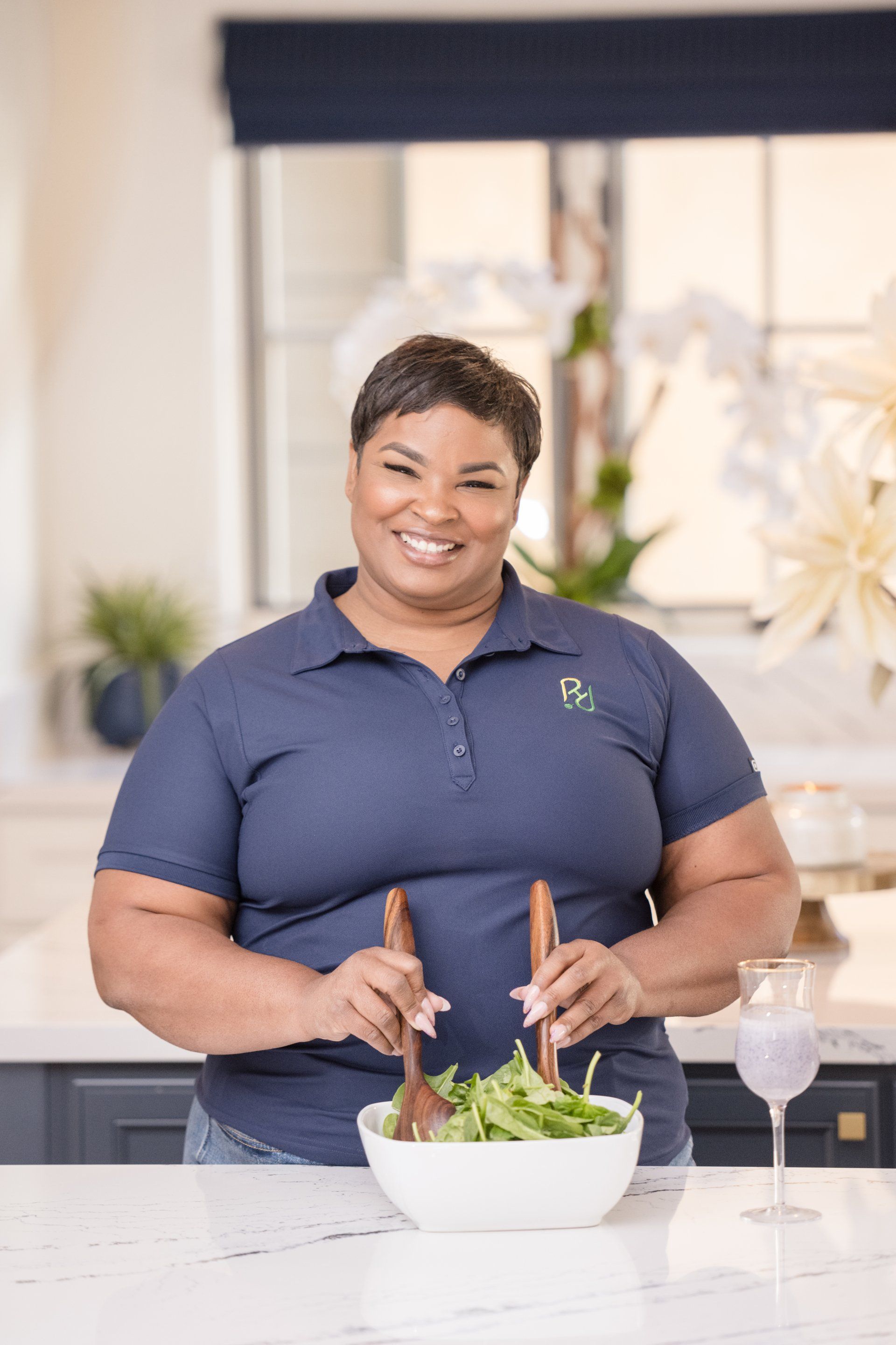 A woman is standing in a kitchen holding a bowl of salad.
