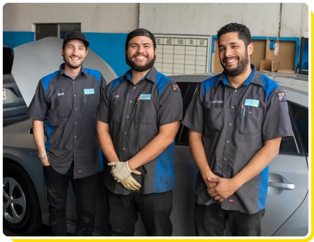 Three men are posing for a picture in front of a car in a garage - Sean's Auto Care