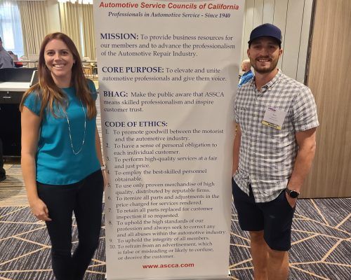 A man and a woman standing next to a sign that says automotive service commission of california