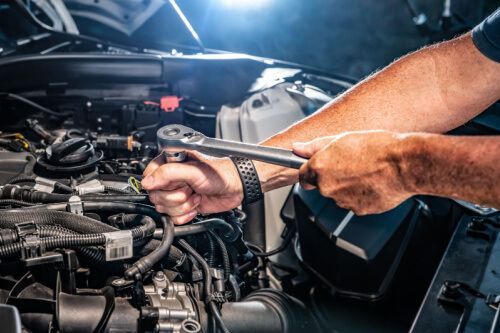 A man is working on a car engine with a wrench - Sean's Auto Care