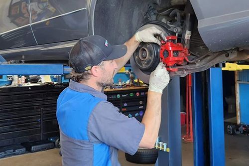 A man is working on the brakes of a car on a lift - Sean's Auto Care