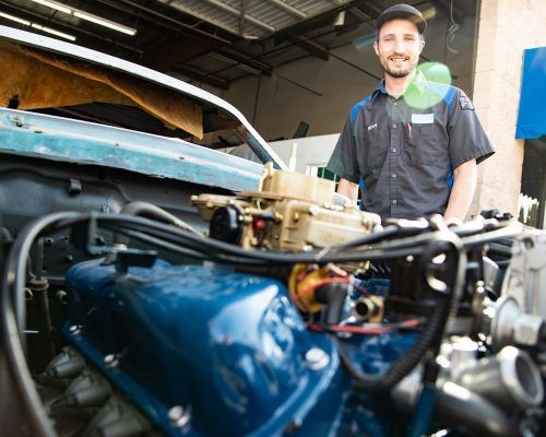 A man is standing next to a car engine in a garage - Sean's Auto Care