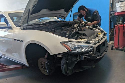 A man is working on a white car with the hood up in a garage - Sean's Auto Care