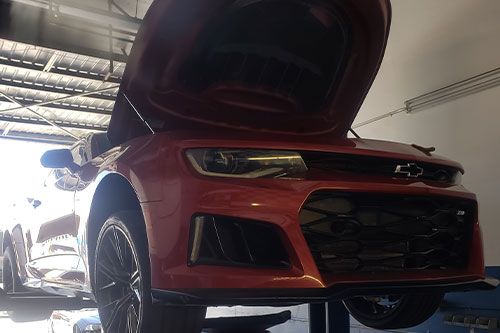 A red car is parked in a garage with the hood up - Sean's Auto Care