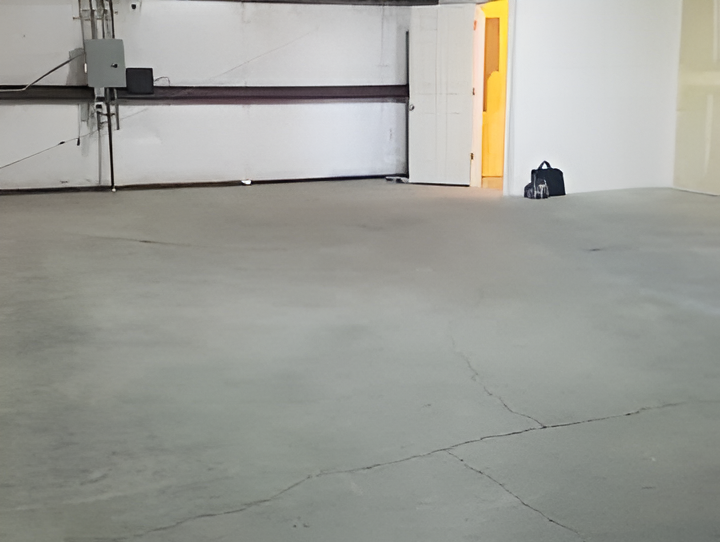 Empty garage with a gray concrete floor, white walls, and a partially open door.
