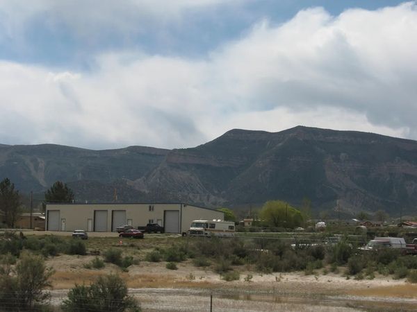 A low building with garage doors sits in a landscape with mountains under a cloudy sky.