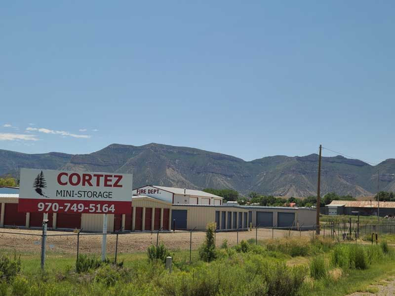 Sign for Cortez Mini-Storage with storage units and mountain backdrop.