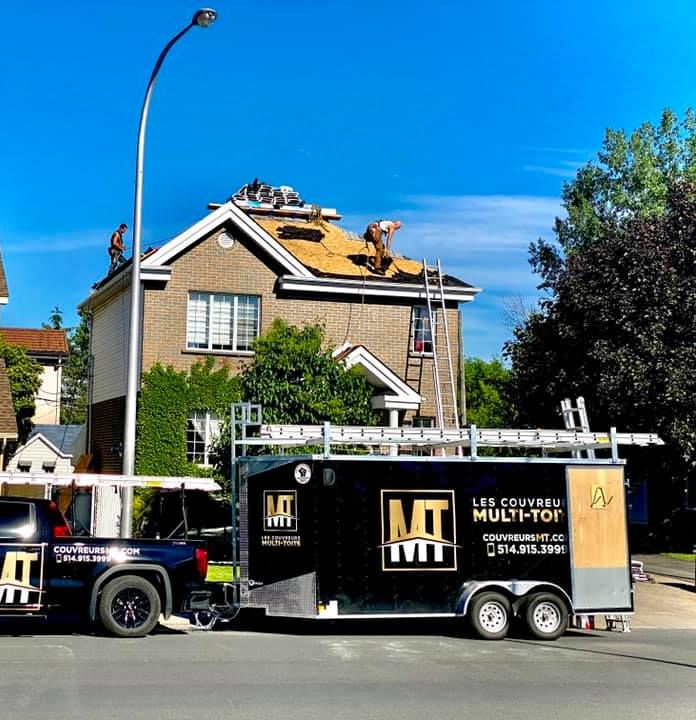Des ouvriers refont le toit d'une maison à côté d'une remorque MT noire dans une rue résidentielle.