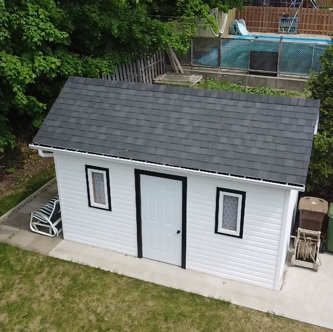 Une vue aérienne d'un hangar blanc avec un toit noir et une piscine en arrière-plan.