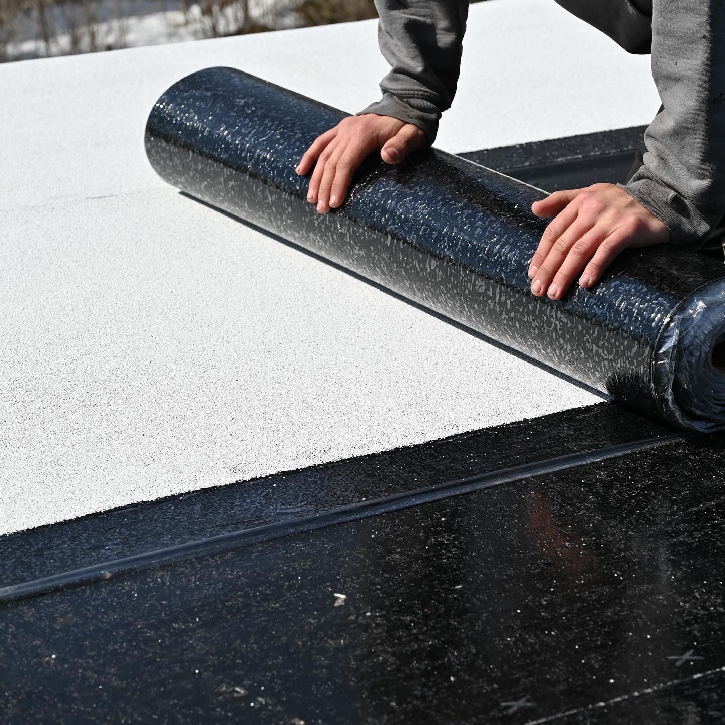 Une personne pose un rouleau de caoutchouc sur un toit