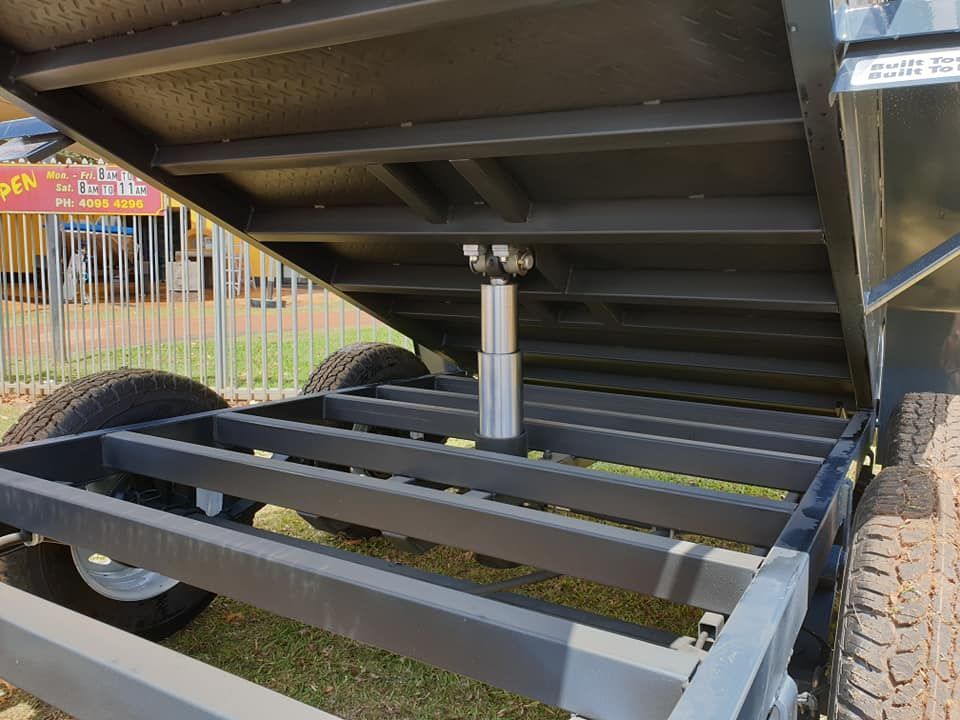 Blue Rollers on a Metal Boat Trailer — Tolga Traders in Tolga, QLD Underside view of a gray trailer with a hydraulic lift, revealing its steel frame and wheels. — Tolga Traders in Tolga, QLD