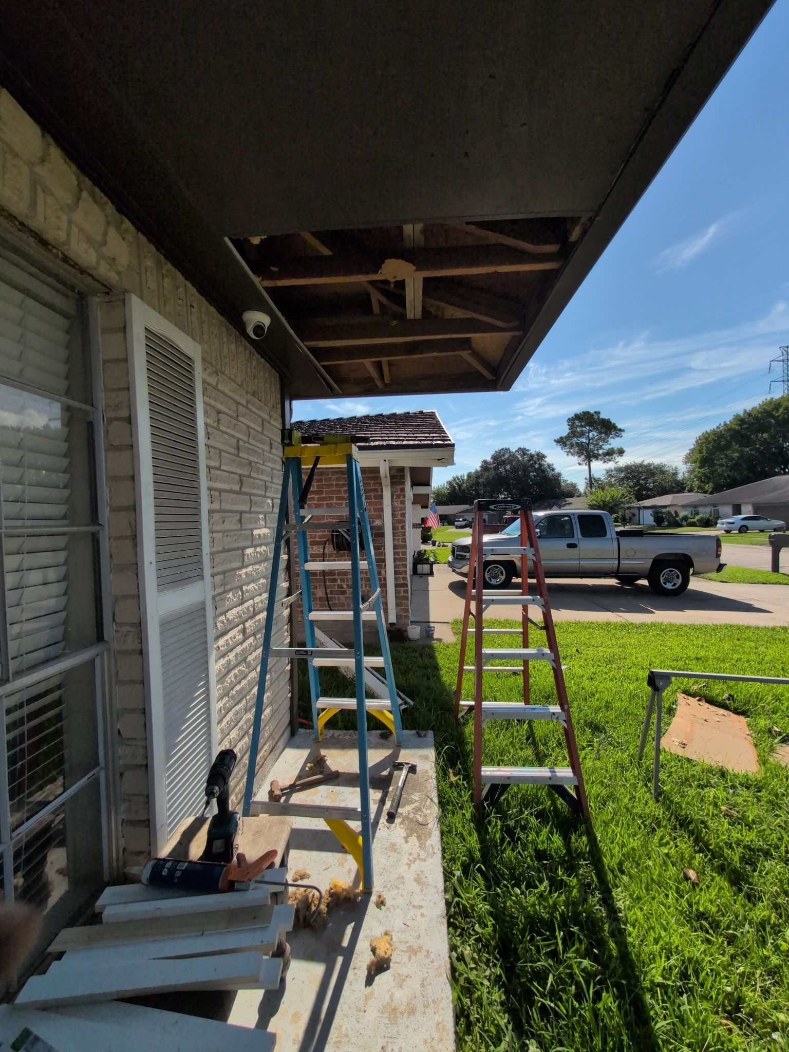Ladders and tools under a house eave during exterior repair, with a truck in the driveway.