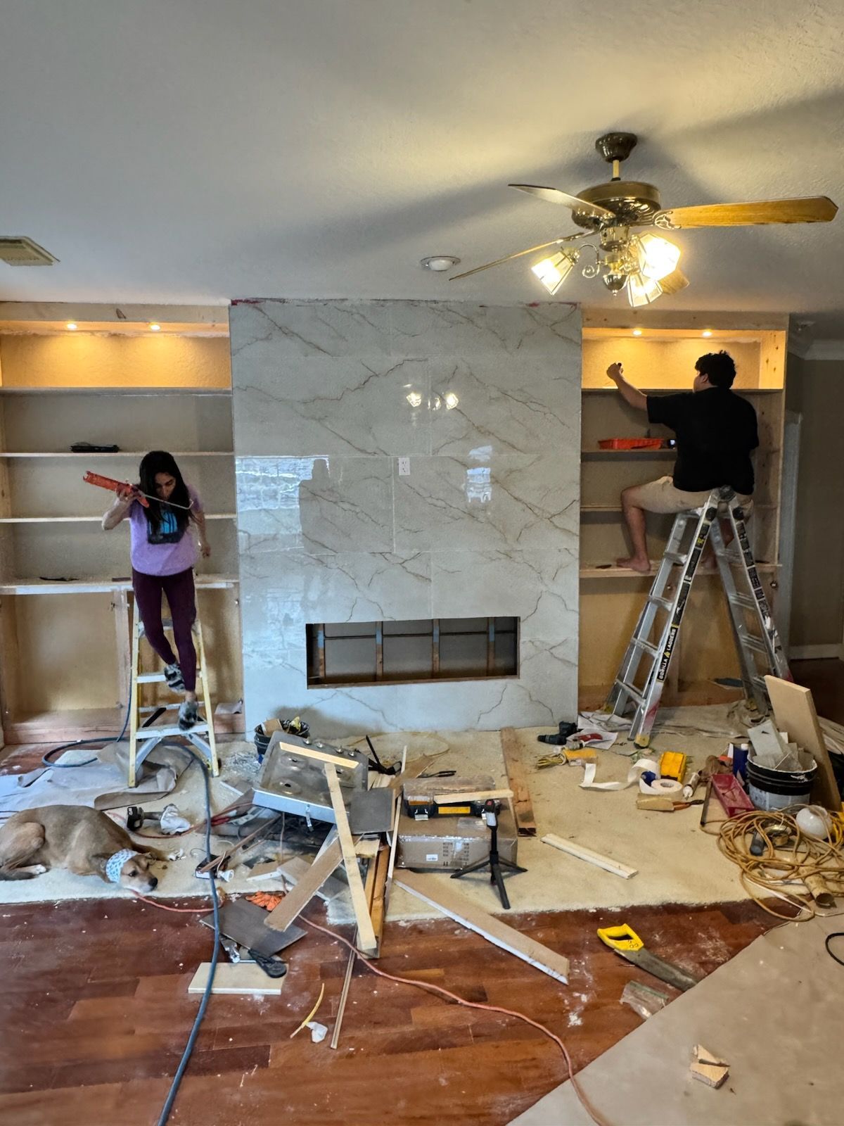 Two workers installing a marble fireplace wall in a living room under renovation