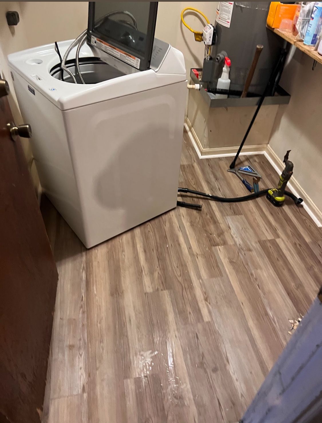 Laundry room with a washing machine, wet floor, and exposed hoses/tools near the wall