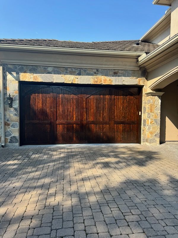 Stone-front house with a dark wooden garage door and paved driveway in sunlight