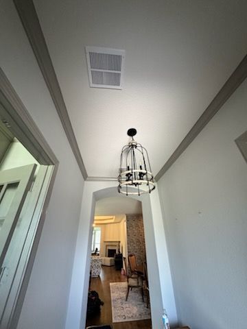 Hallway with high tray ceiling, hanging cage light, white walls, and view into a room beyond