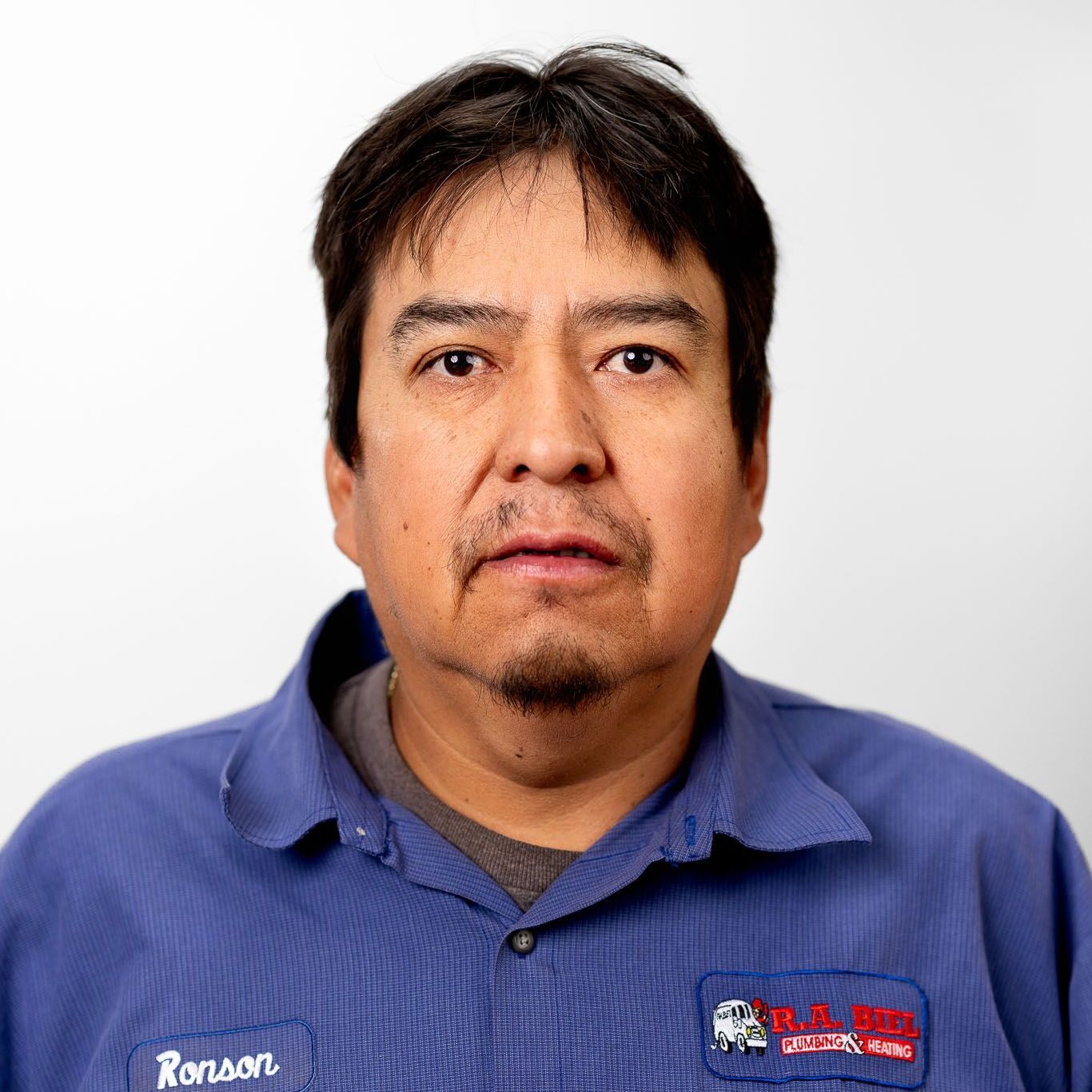 A man in a blue shirt is standing in front of a white background.