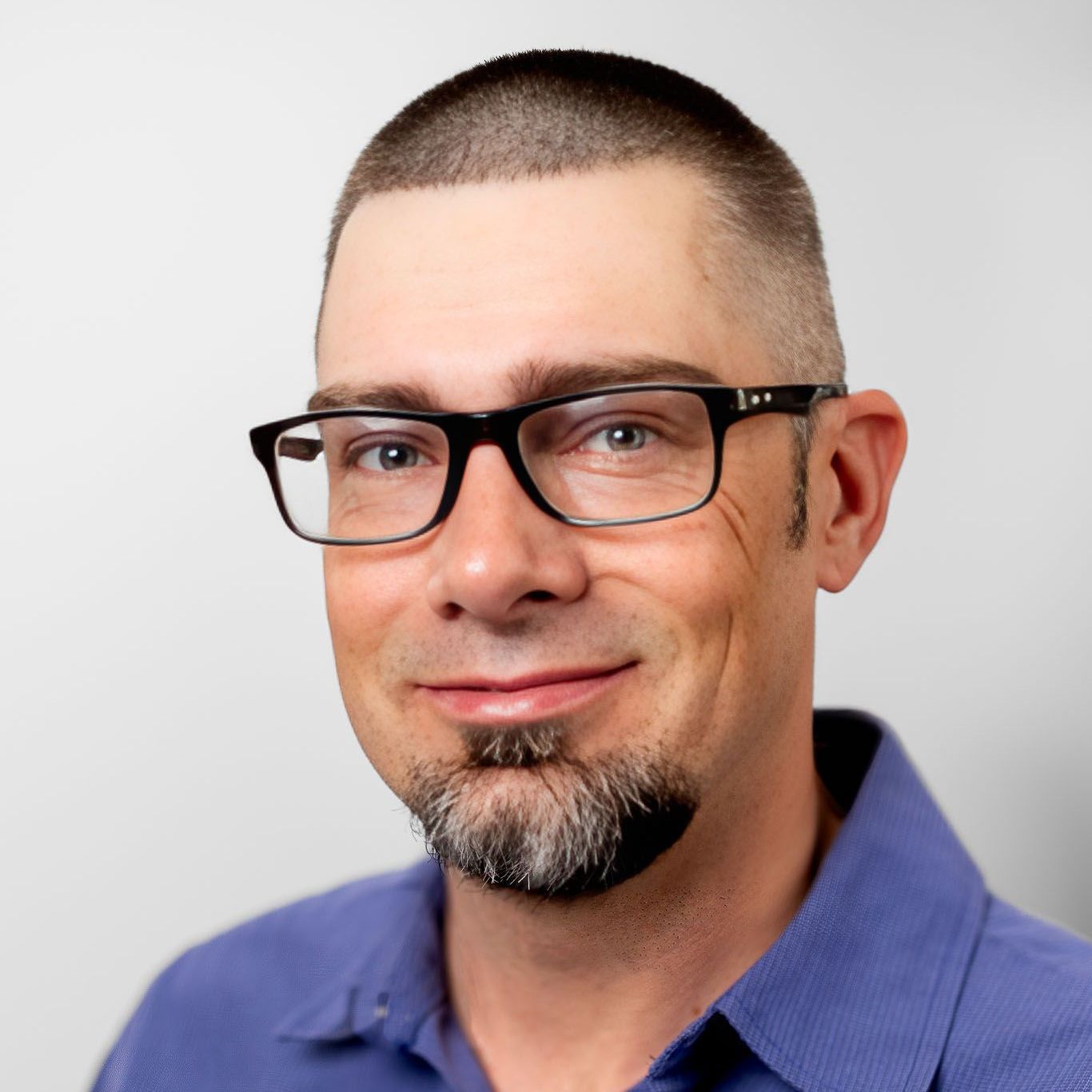 A man wearing glasses and a hat is standing in front of a white wall.